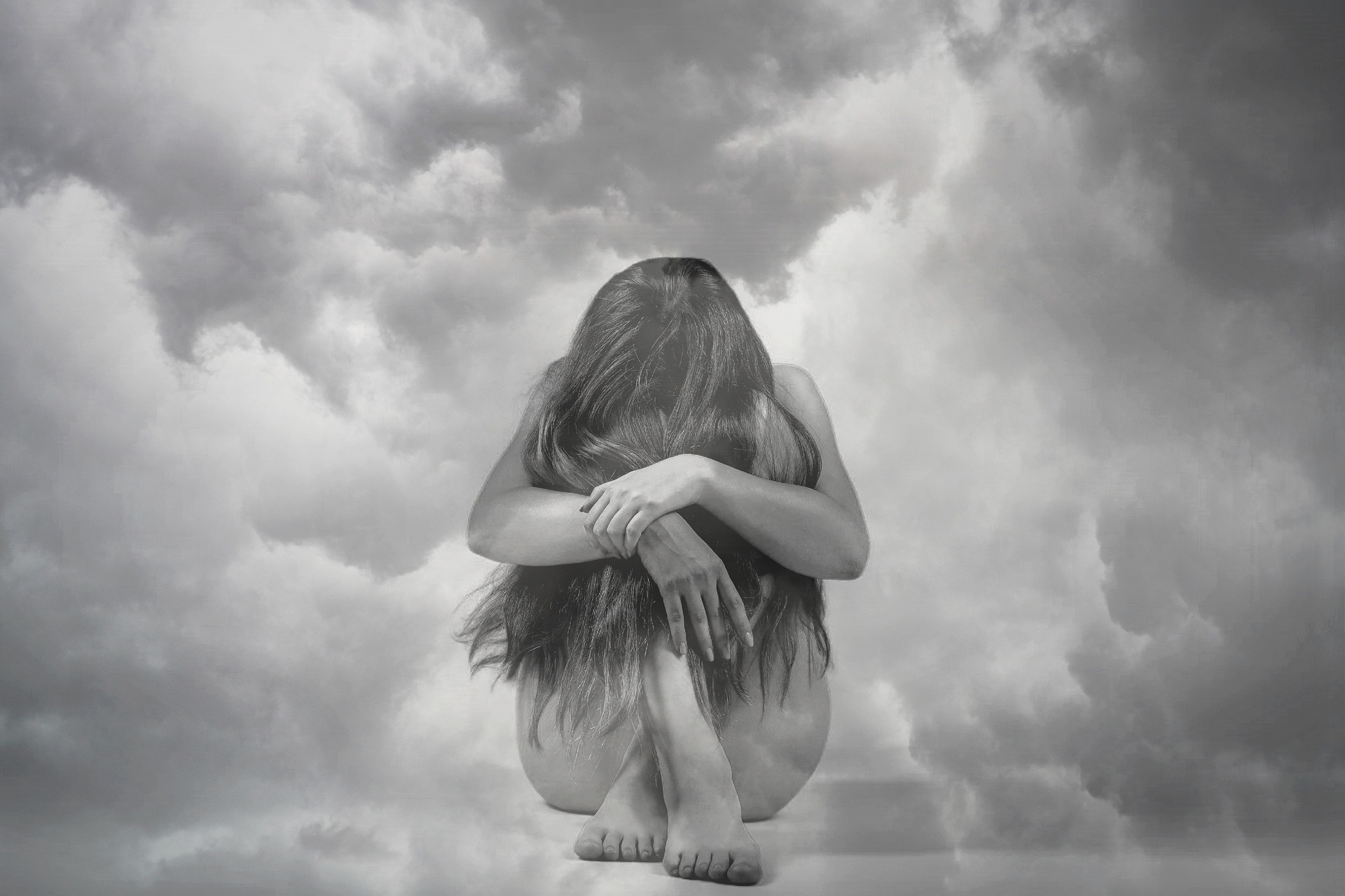 Woman with head on knees against dark clouds